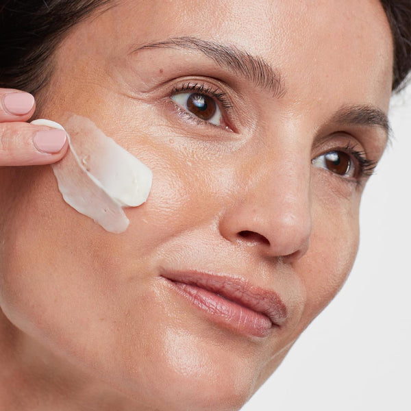 Close-up of a woman gently applying a creamy skincare product to her cheek, showcasing smooth, hydrated skin using Power Luxe | HydroPeptide.