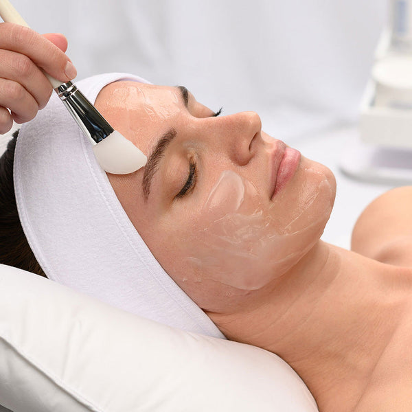 Woman receiving a gentle facial treatment with a soft brush applying a clear skincare mask while wearing the Hydro-Lock Sleep Mask | HydroPeptide for enhanced skin hydration and wellness.