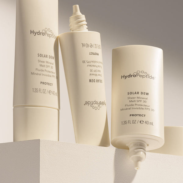 Three beige tubes of Solar Dew SPF Mineral Serum | HydroPeptide displayed on a light surface with minimalist branding and clean design, emphasizing skincare and sun protection.