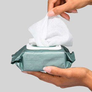 Hands pulling a single white cloth from an open pack of Hydroactive Cleanse Cloths - 30 Pack | HydroPeptide on a light gray background, highlighting skincare cleansing wipes.