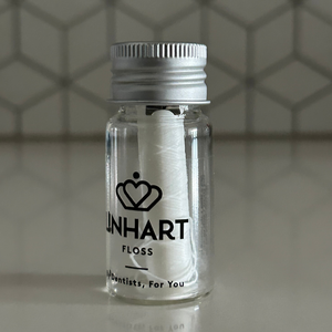 Clear glass jar with a metal screw cap containing white microfiber floss branded "Microfiber Floss | LINHART" displayed on a smooth surface against a hexagonal tiled background.