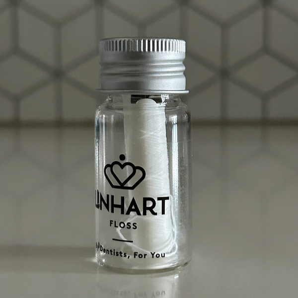 Clear glass jar with a metal screw cap containing white microfiber floss branded "Microfiber Floss | LINHART" displayed on a smooth surface against a hexagonal tiled background.