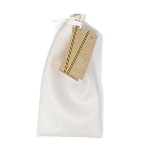 White textured drawstring pouch with a brown tag attached, containing the Rose Quartz Gua Sha | Vie Healing skincare tool inside for wellness and facial massage.