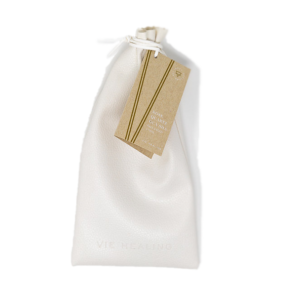 White textured drawstring pouch with a brown tag attached, containing the Rose Quartz Gua Sha | Vie Healing skincare tool inside for wellness and facial massage.