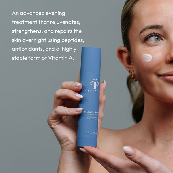 Woman holding a blue bottle of Nighttime Repair Retinol Cream | Circadia with a small amount of cream applied on her cheek, promoting skincare for rejuvenation and repair overnight.