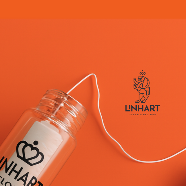 Clear plastic container with white floss partially extended against an orange background, showcasing Microfiber Floss | LINHART for dental care and wellness.