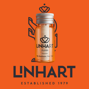 Clear small orange bottle with silver cap containing white microfiber dental floss, branded with "LINHART," set against an orange background with the text "LINHART Established 1979", showcasing Microfiber Floss | LINHART for oral wellness.