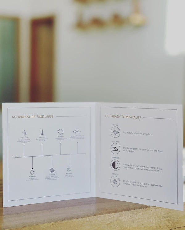 Instructional booklet open on a wooden surface displaying acupressure time lapse chart and step-by-step guidance to use the Linen Acupressure Mat | Vie Healing for wellness and relaxation.