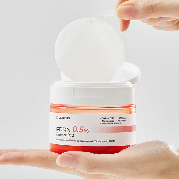 Hand holding an open container of PDRN 0.5% Essence Pad | Leaders with a white pad being lifted out, showcasing skincare product for moisturizing and firming.