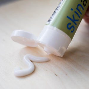 Close-up of a tube dispensing white cream on a wooden surface, showcasing Illuminating Body Peel Cream | Skin Authority for skincare and body care routines.