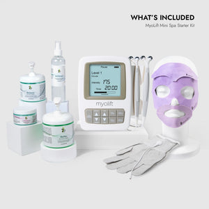 Complete set of skincare products, a digital microcurrent device with handheld probes, a purple facial treatment mask on a mannequin head, and white treatment gloves, part of the Mini Spa Starter Microcurrent Facial Kit | 7e Wellness.