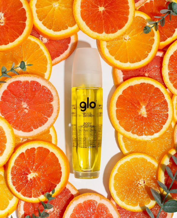 Bottle of Oil910 | Glo910 body sculptor oil surrounded by fresh citrus slices, highlighting natural ingredients for skincare and wellness.