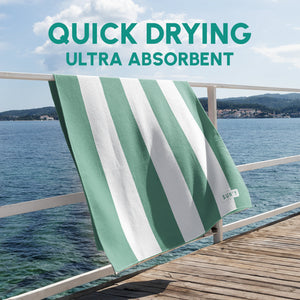 Waffle Microfiber Beach Towel - Sea Green | SUN'Y hanging on a wooden railing by the water, showcasing its quick drying and ultra absorbent fabric with green and white stripes.