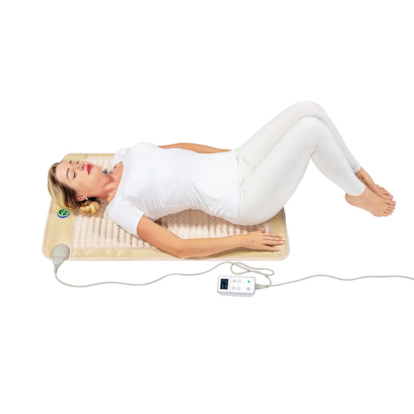 Woman relaxing on a beige wellness mat with controller, demonstrating use of the SOFT Mat Medium 4024 InfraMat Pro® | HealthyLine for body care and recovery.