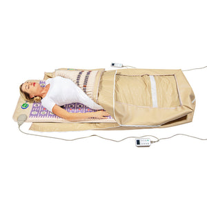Woman lying relaxed on a wellness device with a beige therapeutic mat and blanket, using the TAJ-Mat™ Full 7224 Firm - Photon PEMF InfraMat Pro® | HealthyLine for body care and recovery.