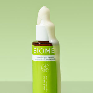 Close-up of a green BIOME+ dew bright serum | IMAGE Skincare bottle with creamy serum overflowing from the top against a soft green background, showcasing skincare product texture.