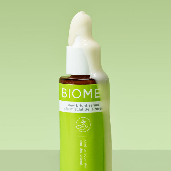 Close-up of a green BIOME+ dew bright serum | IMAGE Skincare bottle with creamy serum overflowing from the top against a soft green background, showcasing skincare product texture.