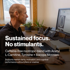 Man concentrating on a computer screen displaying a brain scan in a professional office setting, illustrating mental focus and cognitive performance with Brain Drive wellness supplement.