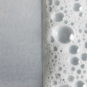 Close-up of bubbly foam texture with water droplets on a smooth surface illustrating the rich lather of Cleansing Foam | Omorovicza for skincare.