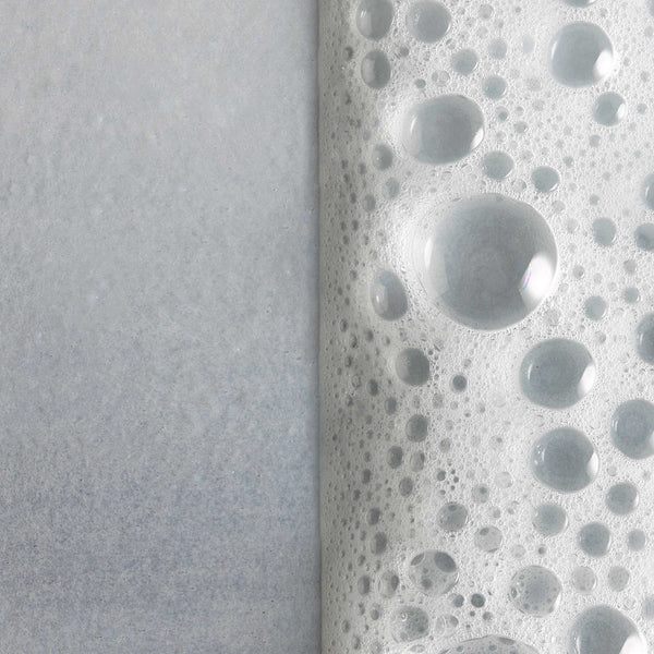 Close-up of bubbly foam texture with water droplets on a smooth surface illustrating the rich lather of Cleansing Foam | Omorovicza for skincare.