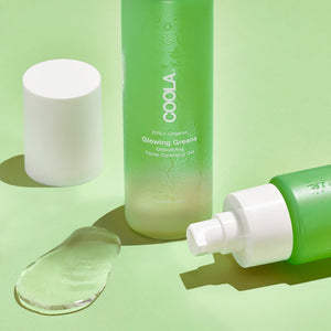 Glowing Greens Detoxifying Facial Cleansing Gel | COOLA in green frosted bottles with clear gel texture on a light green background, showcasing a skincare product for detoxifying and cleansing.