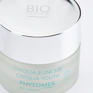 Close-up of a frosted glass jar with a shiny silver lid containing Cyfolia Youth Glow Renewing Wrinkle Cream | Phytomer, a certified organic skincare product.