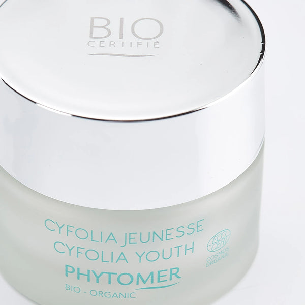 Close-up of a frosted glass jar with a shiny silver lid containing Cyfolia Youth Glow Renewing Wrinkle Cream | Phytomer, a certified organic skincare product.