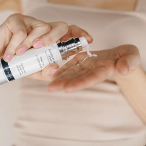Close-up of hands dispensing a small amount of Mindful Moisturizer | DermaplanePro skincare product from a white pump bottle onto the palm, highlighting body care and wellness.