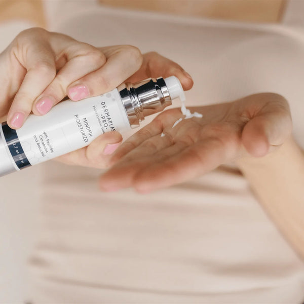 Close-up of hands dispensing a small amount of Mindful Moisturizer | DermaplanePro skincare product from a white pump bottle onto the palm, highlighting body care and wellness.