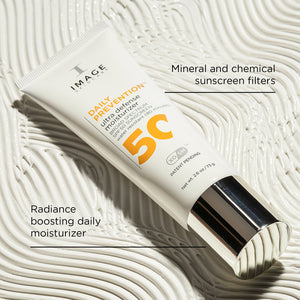 Tube of DAILY PREVENTION Ultra Defense Moisturizer SPF 50 | IMAGE Skincare with a silver cap placed on textured white background highlighting its radiance boosting and mineral and chemical sunscreen features.