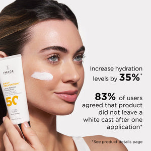 Woman holding DAILY PREVENTION Ultra Defense Moisturizer SPF 50 | IMAGE Skincare with a white cream swatch on her cheek, highlighting hydration and no white cast claims.