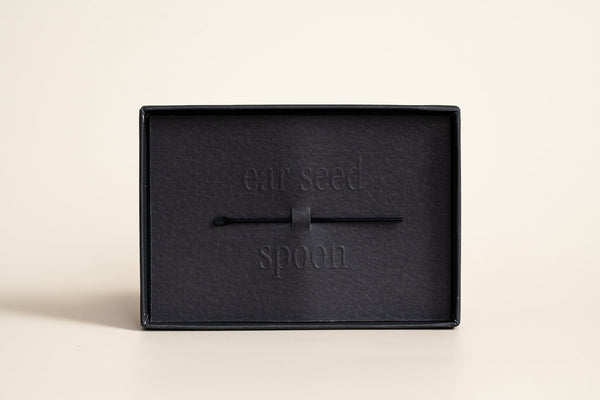 Black ear seed spoon tool resting inside a black box with embossed text, designed for use with Pain Conrol - 24K Gold Ear Seed | Vie Healing.