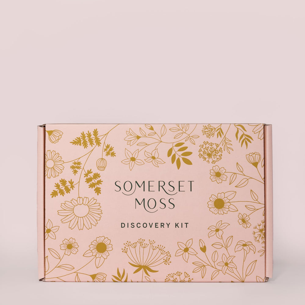 Open gift box displaying Discovery Kit | Somerset Moss skincare products, including tubes and bottles, with a soft drawstring pouch and a message inside the box about simplicity and wellness.