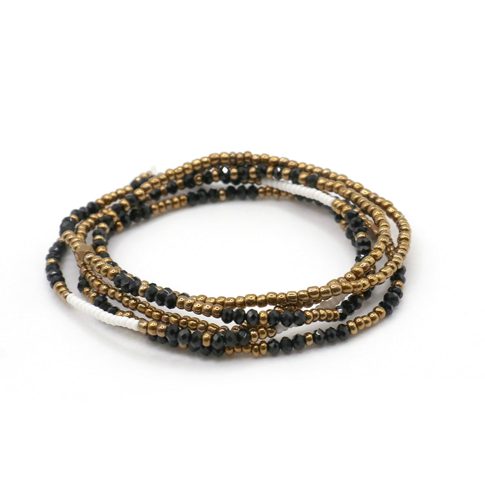 Close-up of a multi-strand stretchy beaded bracelet featuring gold, black, and white beads, designed as the Dusk Stretch Bracelet | Purpose Jewelry for stylish wellness accessories.