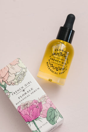 Glass dropper bottle of Florale Botanical Serum | French Girl with yellow liquid beside floral illustrated packaging on light background, skincare product for wellness.