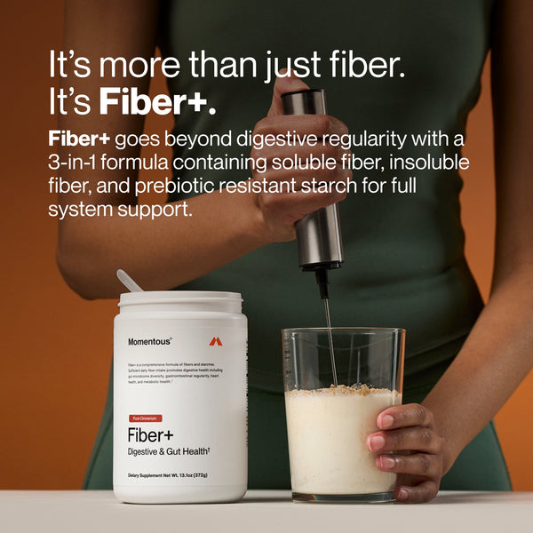 Person holding a blender mixing a glass of supplement powder next to a container of Fiber+ digestive and gut health supplement, promoting fiber for full system support.