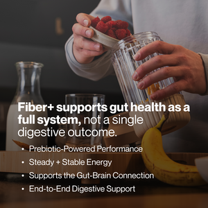 Person holding a container of raspberries over a glass blender with a banana on the counter, promoting Fiber+ 10-Travel Packs for gut health and digestive support.