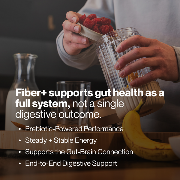 Person holding a container of raspberries over a glass blender with a banana on the counter, promoting Fiber+ 10-Travel Packs for gut health and digestive support.