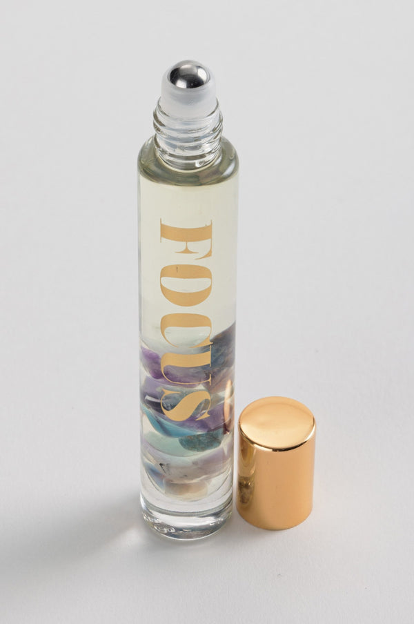 Focus Rollerball | Aluminate Life featuring a clear glass bottle with a metal rollerball applicator and a gold cap, containing a light-colored liquid with decorative stones inside.