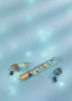 Focus Rollerball | Aluminate Life placed on a soft blue surface surrounded by small polished healing stones, reflecting a calming and wellness-focused atmosphere.