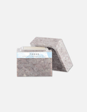 Open textured stone container with a white balm stick inside, featuring minimalist design and natural tones, representing Concreta | Zents skincare product.
