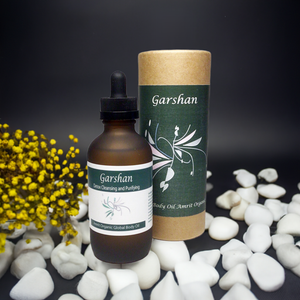 Garshan Body Oil | Red Cherry Group in a brown dropper bottle with green label beside matching cylindrical packaging, surrounded by white stones and yellow flowers on a dark background