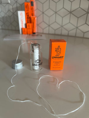 Microfiber Floss | LINHART displayed with an open transparent container and bright orange packaging on a modern tiled countertop, emphasizing oral care and wellness.