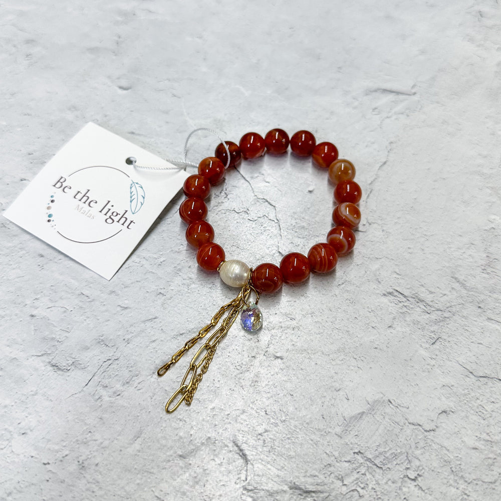 Carnelian Luxe Bracelet | Be the Light featuring polished red carnelian beads, a single pearl accent, and delicate gold chain tassels on a textured light background.