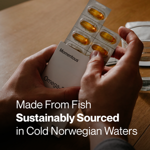 Hands holding a blister pack of golden capsules partially inserted into a white box labeled Omega-3 Travel Packs, emphasizing sustainably sourced fish oil from cold Norwegian waters.