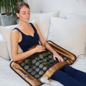 Woman relaxing on a couch using the Mesh JT Pad Medium 3220 Soft InfraMat Pro® | HealthyLine for wellness and recovery with jade tourmaline stones and heat therapy.