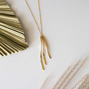 Kailani Necklace | Purpose Jewelry featuring a delicate gold chain with three slender, curved gold pendants displayed on a minimalist white background with natural decorative elements.
