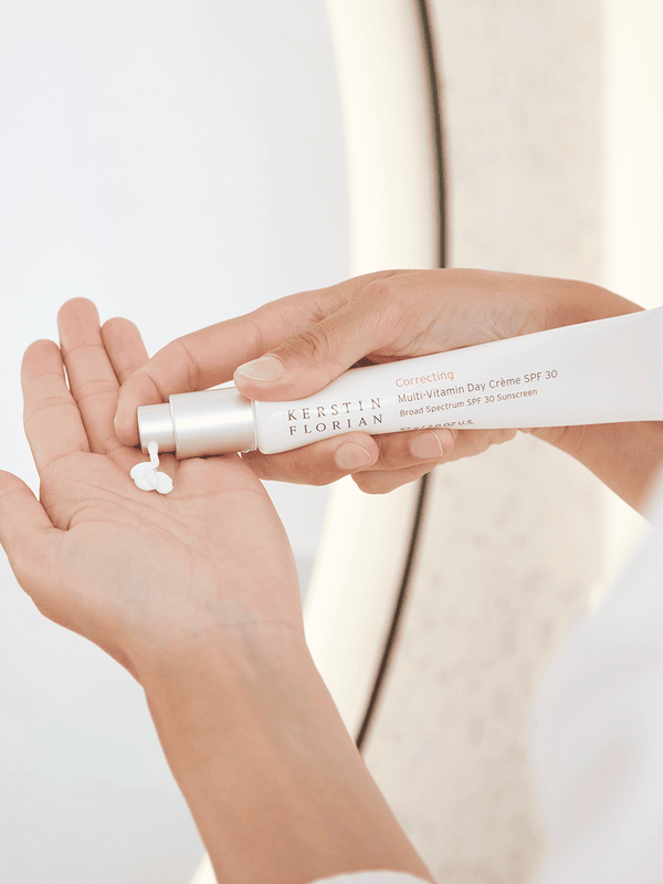 Person dispensing white cream from a tube labeled Correcting Multi-Vitamin Day Creme | Kerstin Florian into their palm, demonstrating skincare application with a neutral background.