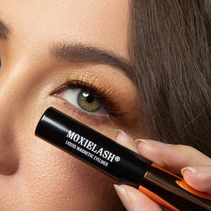Close-up of a woman holding a tube of Magnetic Liquid Eyeliner | Moxielash near her eye, showcasing flawless makeup with shimmering gold eyeshadow and natural eyelashes.