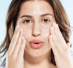 Close-up of a woman gently applying skincare cream to her face, illustrating the moisturizing benefits of the Silky, Milky & Most Loved Naked Nourishment Set | Farmhouse Fresh for radiant skin.